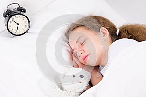 The girl is sleeping with an alarm clock, hugging