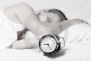 Girl is sleeping in bed and is switching alarm clock. sleepy woman holds alarm clock in her hand and sleeps