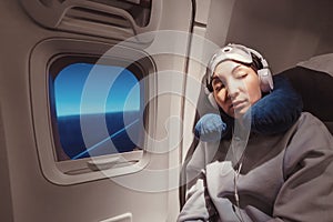 girl sleeping in her seat on the plane near the window in a mask and with a pillow to sleep. The concept of travel with