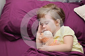 Girl sleeping peacefully with her teddy bear on the bed