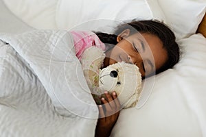 Girl sleeping with teddy bear in bed in bedroom