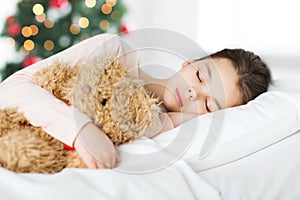 Girl sleeping with teddy bear in bed at christmas