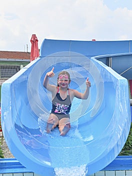 Girl sliding down on a water slide into plunge pool in aqua park. Vacation concept. Holiday fun