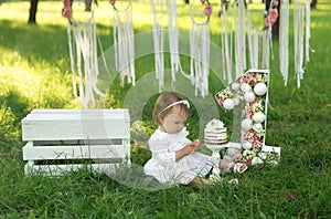 A girl in a smart white dress is sitting on the grass and looking at her hands soiled in cream.