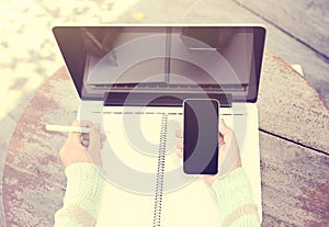 Girl with smartphone, blank diary with pen and laptop on a woode