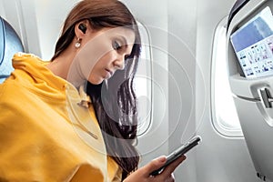 A girl with a smartphone in front of an airplane window, the cabin of a passenger airliner. Using gadgets in flight, airplane mode