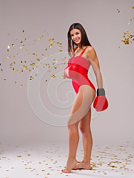 The girl with a smile stands sideways in boxing gloves on a gray background with flying sparkles