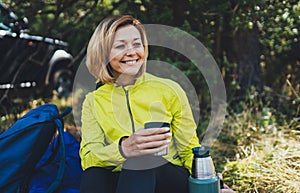 Girl smiles and enjoys breakfast outdoors summer nature, tourist hold hand mug of warm tea during recreation trip, happy hiker