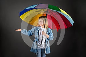 The girl smiles, holds a multicolored rainbow umbrella in her hands and checks if it is raining