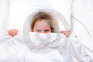 girl with smiling eyes in bed hiding under the covers