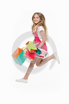 Girl on smiling face carries bunches of shopping bags, isolated on white background. Kid girl with long hair fond of