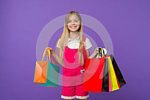 Girl on smiling face carries bunches of shopping bags, isolated on white background. Girl likes to buy fashionable