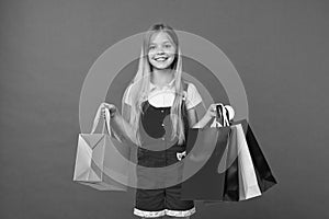 Girl on smiling face carries bunches of shopping bags, isolated on white background. Girl likes to buy fashionable