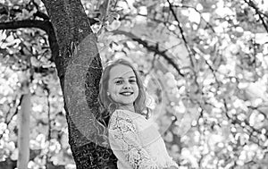 Girl on smiling face standing near sakura, lean on tree trunk. Girl with long hair outdoor, cherry blossom or sakura on