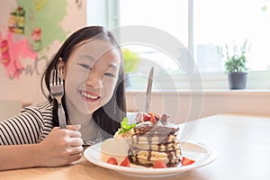 Girl is smiling happily,holding a knife and fork is preparing to eat pancakes in restaurants photo