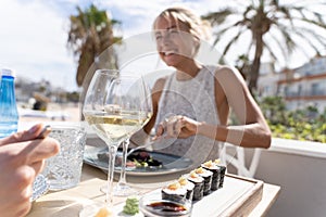 Girl smiling out of focus with two glasses of white wine adn pieces of shushi with soy sauce served with a piece of wood