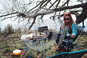 Girl smokes a hookah on the nature. Camping outdoor recreation. Lake on background. Portable, folding equipment for hiking trips.