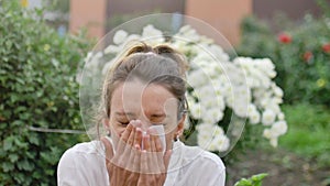 Girl sneezes into a napkin, because she is allergic to flowering during spring time on white chrysanthemums on