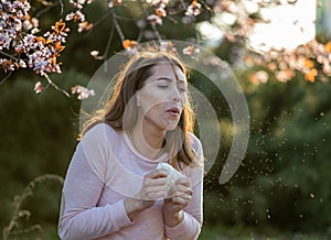 Girl sneezing in front of blooming tree in spring