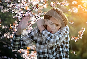 Girl sneezing in front of blooming tree in spring