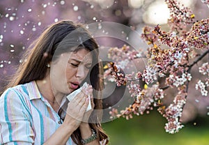 Girl sneezing in front of blooming tree in spring