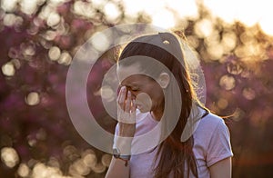 Girl sneezing in front of blooming tree in spring