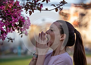 Girl sneezing in napkin in front of blooming tree in spring