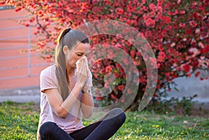 Girl sneezing in napkin in front of blooming tree in spring