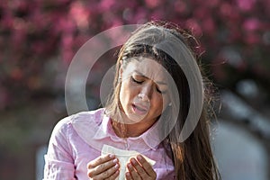 Girl sneezing in napkin in front of blooming tree in spring