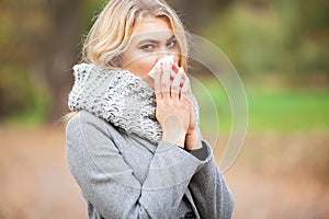 Girl sneezing in tissue. Young woman blowing her nose on the park. Woman portrait outdoor sneezing because cold and flu