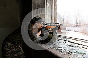 Girl sniper looks through the scope. Girl warrior directs his rifle through the broken window of an abandoned building. Military