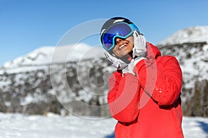 Girl snowboarder in a helmet and mask holds her palms to her face and smiles. Sheregesh resort