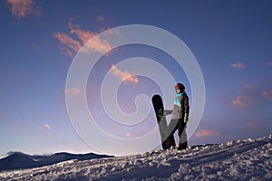 Girl snowboarder stands on a hillside against dark sunset sky