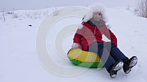 Girl on snowy plate rolls down from high snowy mountain and laughs with pleasure. Teenager plays in winter with sleds