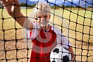 Girl, soccer player and ball on goal net, smile and happy for game, field and child. Outdoor, playful and sport for