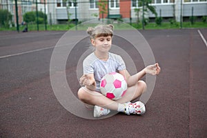 Girl soccer player with a pink soccer ball isolated on a football field or brown background practicing yoga, meditating