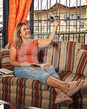 Girl on a sofa reading having fun headphones taking selfie