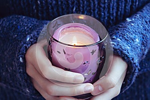 Girl in soft warm dark blue knitted sweater holds in hands burning candle