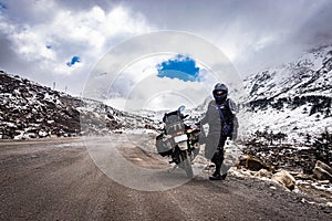 Girl solo ridder in ridding gears with loaded motorcycle at isolated road and snow cap mountains