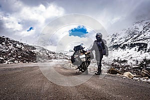 Girl solo ridder in ridding gears with loaded motorcycle at isolated road and snow cap mountains