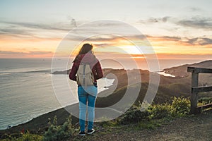 Girl solo traveler watching a beautiful sunset over the Pacific Ocean on top of a hill