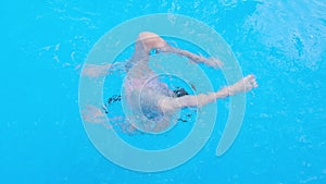 Girl somersaults and plays in the transparent blue swimming pool water. Child have fun in swim pool. Full HD slow motion