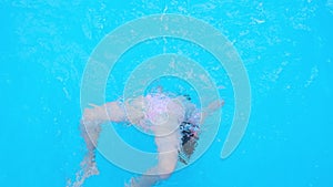 Girl somersaults and plays in the transparent blue swimming pool water. Child have fun in swim pool. Full HD slow motion