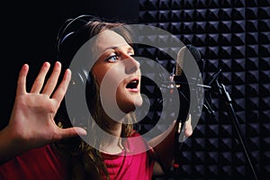 Girl a song in the headphones with hands up. Young woman in red clothes sings into the recording studio. Musician in recording