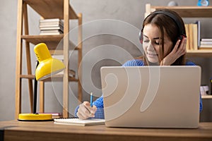 Girl speaking in headphones and writing at notebook. Student woman online larning photo