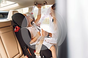 Girl is in a special baby seat. Young woman with her little daughter is with their electric car outdoors