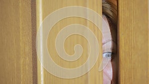 Girl spies through a door crack. Eye looking through a slit
