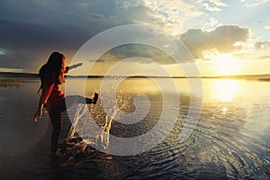 Girl splashing in the water at the lake and watching the beautiful sunset