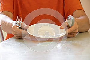 A girl with a spoon and fork and an empty plate sits at the table in the kitchen at home, without food