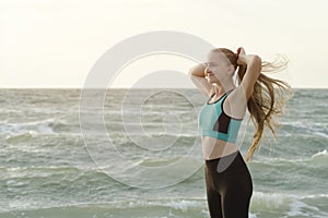 Girl in sports clothes on the beach adjusts her hair. Morning li